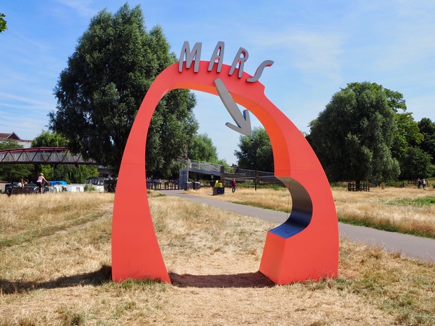 A bright red archway with the title 'Mars', and an arrow pointing towards a small red marble on a string (representing Mars itself, to scale). The string is in a recess carved into the arch.